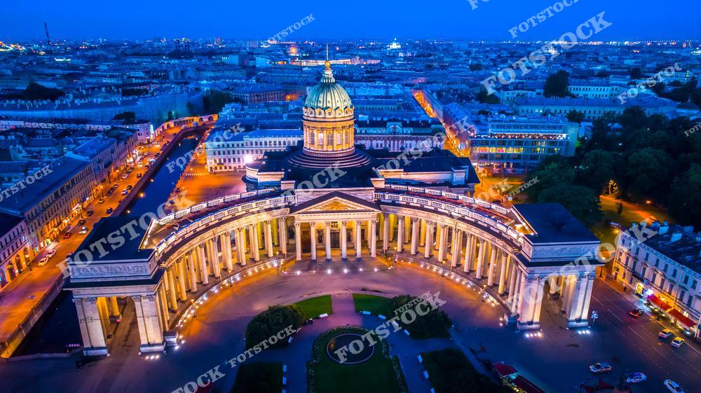 На фотографии изображен Казанский собор в центре Санкт-Петербурга, сияющий в вечерней подсветке. Его величественная колоннада и купол создают выразительный архитектурный облик. Окружающие улицы и парки подчёркивают гармонию городской среды. Ночной свет добавляет снимку атмосферу торжественности и спокойствия.